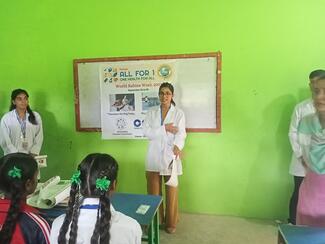 Student volunteer standing in front of classroom giving lecture on rabies awareness infant of a white board on a green wall.